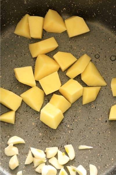 Chopped potatoes and garlic sizzling in a frying pan